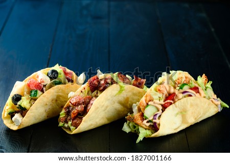 Three Mexican tacos with beef and vegetables on wooden dark background. Mexican dish with sauces guacamole and salsa three mexican pork carnitas tacos flat lay set composition with copy space.
