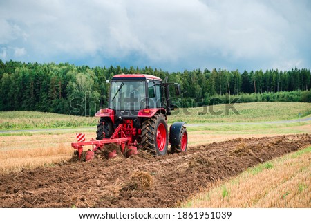 Red Tractor Plowing in Autumn, Farmer plowing stubble field in tractor preparing plows the land, agricultural works at farmlands, agriculture tractor-landscape 商業照片 © 