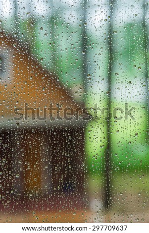Wet glass with raindrops. In the background part of Ã?Â�ountry house in the woods. Focus on raindrops