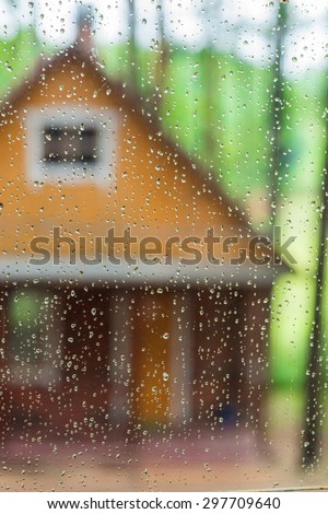 Wet glass with raindrops. In the background part of Ã?Â�ountry house in the woods on a sunny day. Focus on raindrops