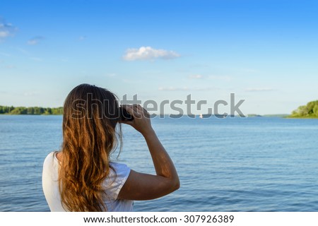 Woman looking through binoculars as a for a bright future, landscape out of focus, focus foreground