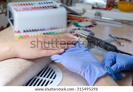 The manicurist holds hands of the client in beauty salon on desktop for manicure with nail polishes