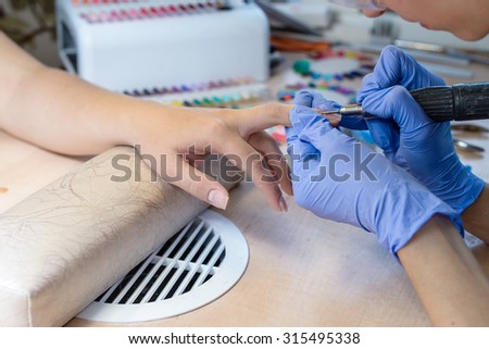 closeup of the hands of a young woman receiving the nail file by a beautician at the beauty salon - focus on the finger