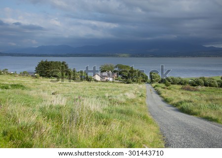 Pastoral landscape showing scenic coastal fields in County Kerry on west coast of Ireland overlooking the Atlantic on a sunny day with green fields and stormy skies with clouds and mountains.