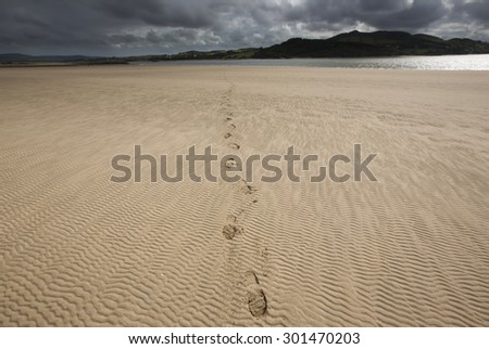 Ireland west coast landscape scene with footprints in rippled  sand during stormy weather in summer on a sandy beach with sun shining through broken cloud.
