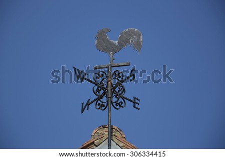 Weather cock or vane on the roof of a white sided building against a blue sky in England UK in summer