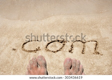 The word .com handwritten in sand on a beach, ideal for internet or conceptual designs background with feet metaphor for communication, speech, message, mail, dialog, talk, contact, email, internet