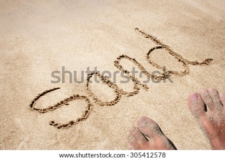 Sand hand written in sand on a beach on an exotic island background with feet for summer