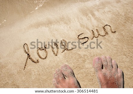 Love sun hand written in sand on a beach on an exotic island background with feet