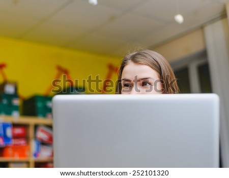 cheerful business young woman looking from behind laptop