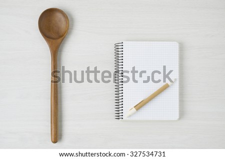 Notepad and wooden spoon on white wood table.