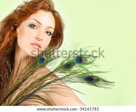Beautiful red-haired women with peacock feathers in studio shot