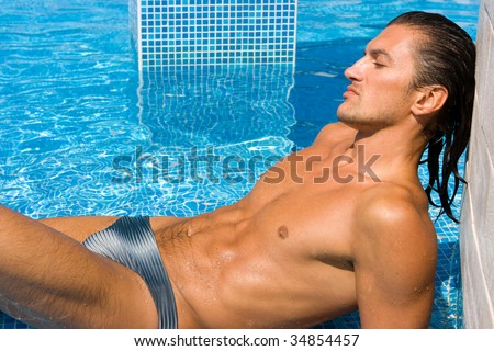 Young wet sexy muscular man lying relaxing in swimming pool