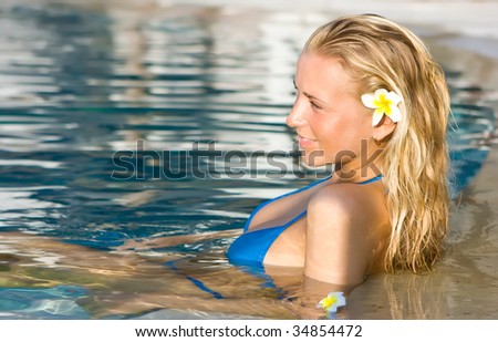 Beautiful blonde girl in hotel swimming pool with flower in long hair