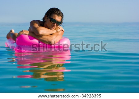 Handsome muscular young man floating on inflatable raft in sea water in sunglasses
