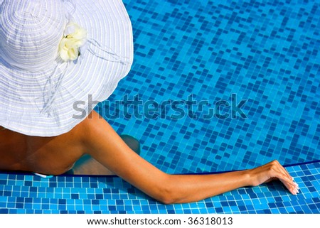 Woman with white hat relaxing in swimming pool in blue water