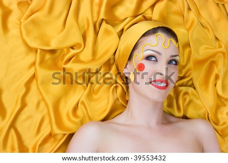 Beautiful female model with bright make-up lying with hair of gold silk in studio shot