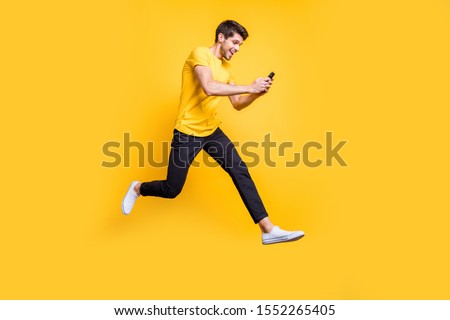 Full body photo of handsome guy jumping high holding telephone rushing romantic date typing girlfriend sms wear casual t-shirt trousers isolated yellow color background