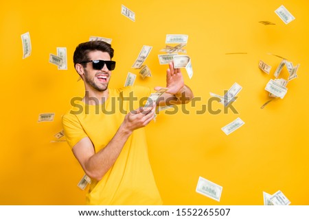 Photo of young handsome careless guy throwing usa money banknotes away wealthy person wear sun specs casual t-shirt isolated bright yellow color background