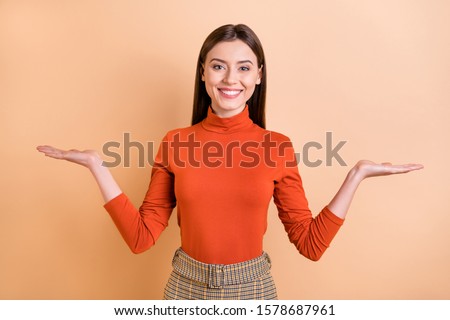 Photo of cheerful charming cute nice girlfriend smiling toothily proposing you to choose something she holds with hands wearing red turtleneck isolated over beige pastel color background Stock foto © 