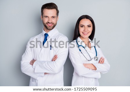 Photo of handsome doc guy lady patient consultation virology clinic stand back-to-back toothy smiling arms crossed experienced doctors wear lab coats isolated grey color background