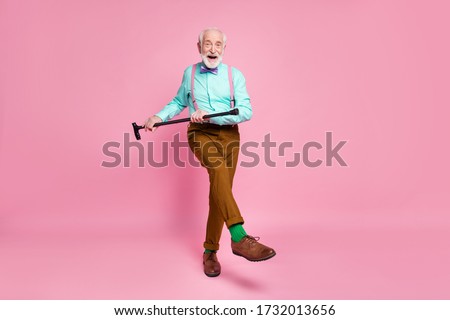 Full length photo of active grandpa moving dance pensioner party use walk stick raise leg wear mint shirt suspenders bow tie pants shoes green socks isolated pink pastel background