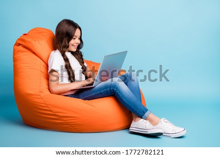 Portrait of nice attractive lovely pretty cute focused cheerful wavy-haired girl sitting in chair using laptop isolated on bright vivid shine vibrant blue teal turquoise color background