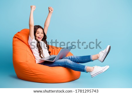 Portrait of nice attractive cheerful cheery excited glad wavy-haired girl sitting in chair using laptop celebrating win isolated on bright vivid shine vibrant blue teal turquoise color background