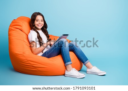 Portrait of nice attractive lovely pretty smart cheerful wavy-haired girl sitting in chair using reading ebook isolated on bright vivid shine vibrant blue teal turquoise color background