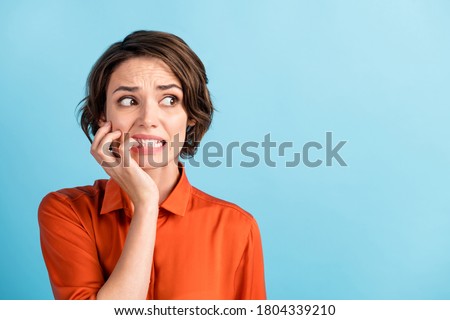 Oops. Closeup photo of sad terrified lady horrified facial expression made big mistake feel guilty look side empty space bite lips fingers wear orange shirt isolated blue color background