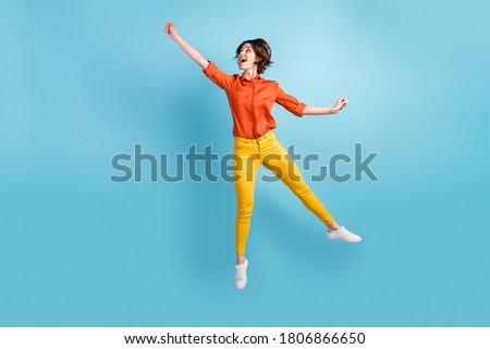 Full body photo of attractive funny lady jump high flight raising up air imaginary umbrella rejoicing weekend wear orange shirt yellow trousers sneakers isolated blue color background Stock foto © 