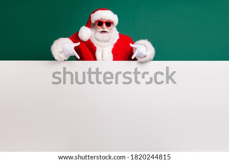 Photo of retired stylish grandfather grey hair beard direct finger white empty board offer present wear red santa x-mas costume coat gloves sunglass headwear isolated green color background 商業照片 © 