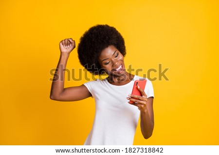 Photo portrait of young woman celebrating victory holding one fist up wearing casual white t-shirt isolated on vivid yellow colored background