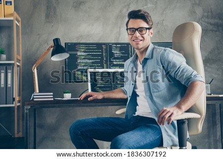 Portrait of positive guy it specialist sit chair desk enjoy working pc home ready debugging java script cyber space error wear denim jeans shirt in workplace
