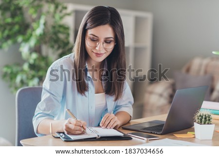 Photo of pretty young girl sit desktop pc hold pen write notepad wear glasses shirt in home office indoors Foto d'archivio © 