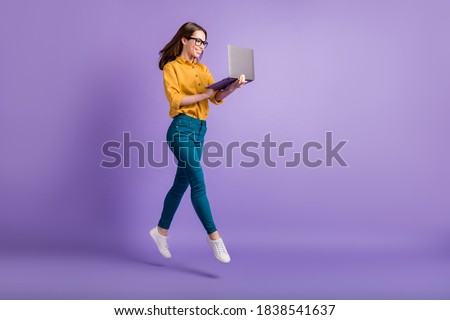 Full length profile photo of lady jump hold netbook look screen wear yellow shirt blue pants sneakers isolated violet color background