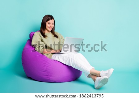 Photo portrait full body view of woman typing on laptop sitting in purple armchair isolated on vivid turquoise colored background