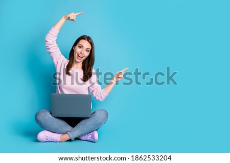 Full body photo girl sit floor legs crossed work laptop point index finger copyspace direct way follow comment ads wear lilac violet pullover denim jeans isolated blue color background