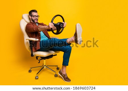 Full length body photo of happy fooling man in chair keeping steering wheel pretending car driver isolated vivid yellow color background