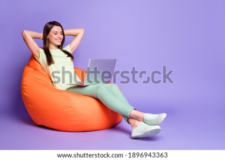 Photo portrait full body view of girl relaxing with laptop hands behind head in bean bag chair isolated on vivid violet colored background