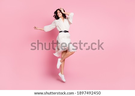 Full length body size photo of cheerful woman in long dress jumping looking empty space isolated pastel pink color background