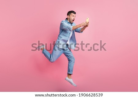 Full body photo of brunette man hold phone amazed news run jump wear casual outfit isolated on pink color background
