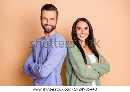 Back-to-back photo of young happy smiling cheerful couple of friends with crossed hands isolated on beige color background