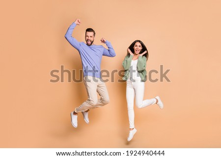 Full length body size view of nice cheerful lucky partners couple jumping having fun isolated on beige pastel color background