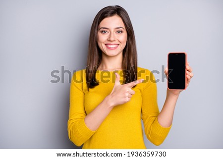 Portrait of pretty content cheerful girl holding in hand demonstrating gadget advert isolated over grey color background