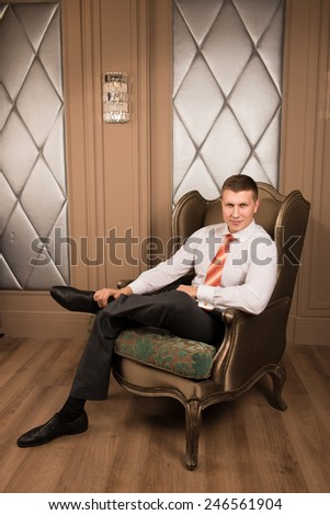 confidence handsome businessman in chic interior. Successful young man in a business suit sitting on the armchair with his legs crossed and smiling
