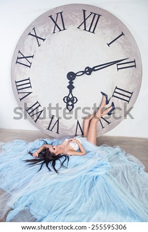 girl in a  long dress with plume lying on the floor on her dress near the huge clock