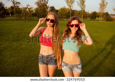 Two young slim girls holding hands and glasses in the park