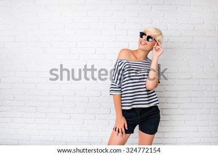 Funny young woman with glasses smiling standing near brick wall