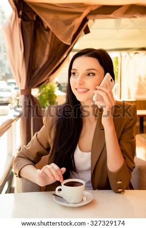 Young cherful woman talking on phone at dinner with cup of coffee